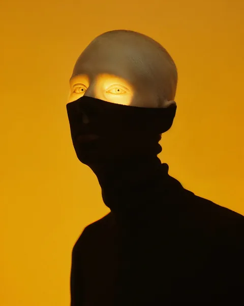 Ein verhülltes Gesicht mit gelb leuchtenden Augen vor orangefarbenem Hintergrund.